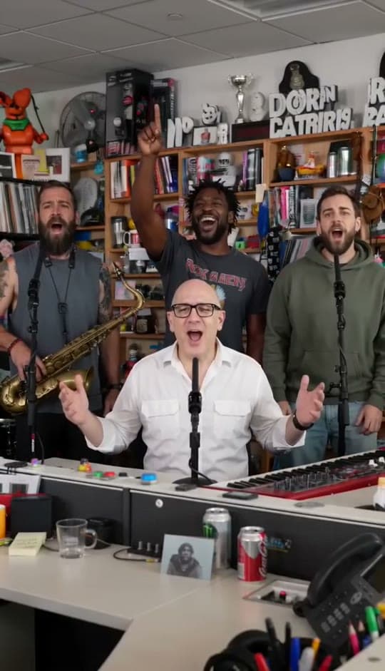 The band finale of a Tiny Desk AI sample video with all four singers and the sax player at the desk